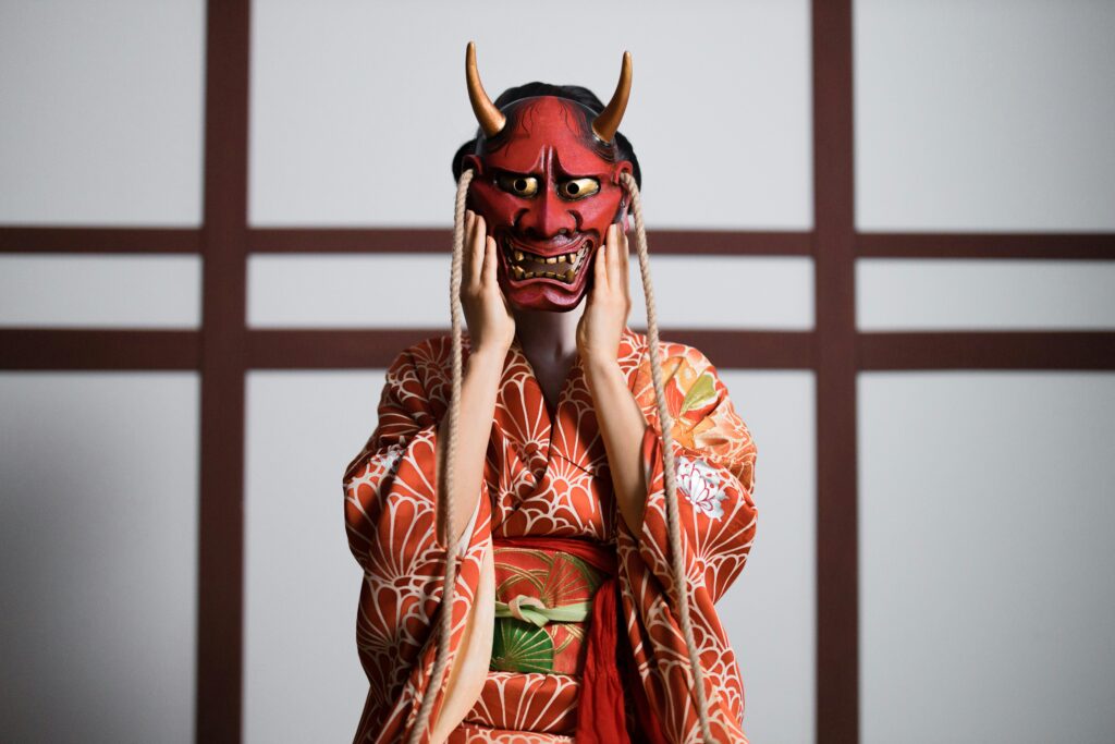 Person in a traditional Japanese kimono wearing a red Hannya mask with horns.