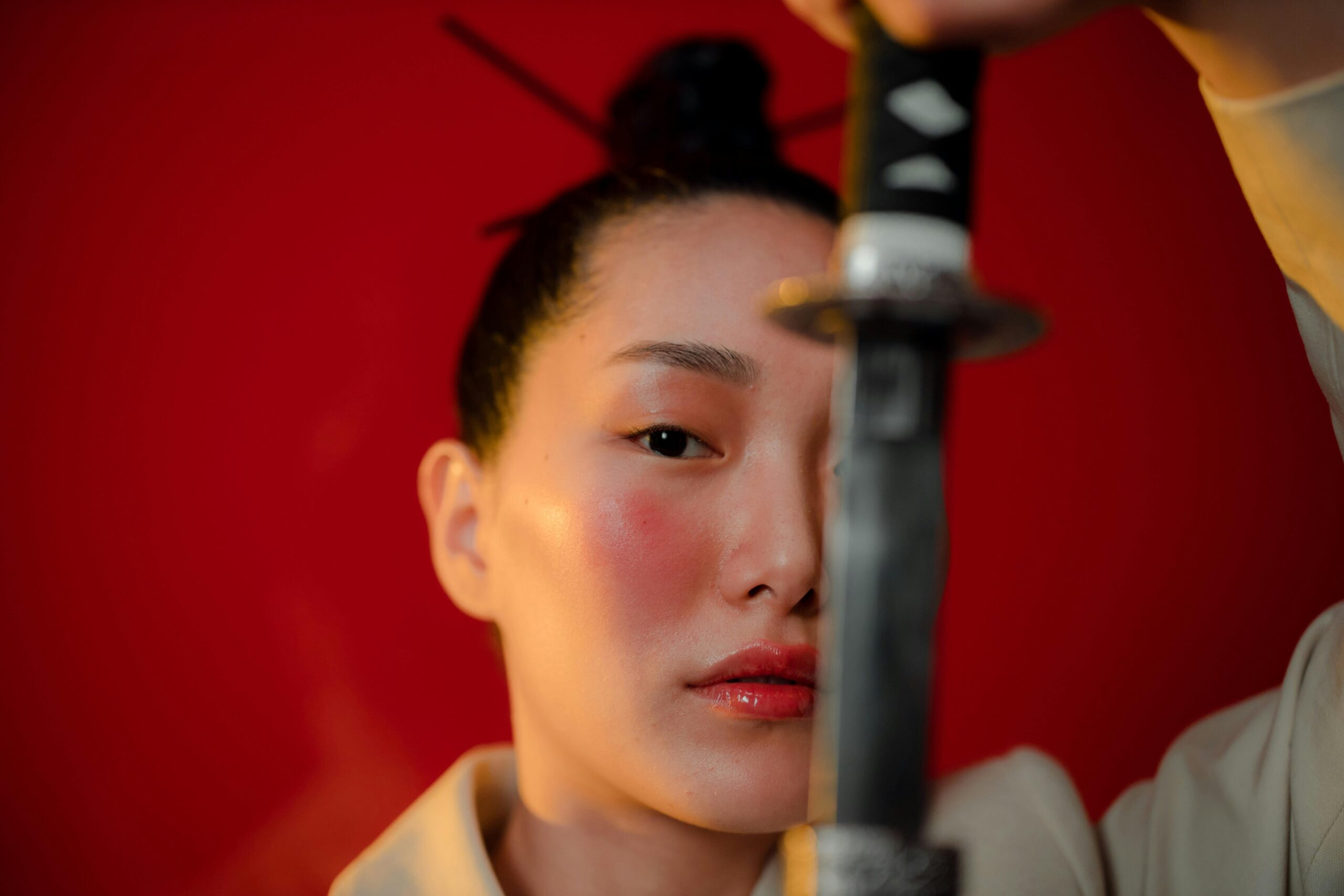 Close-up of a serious woman holding a katana in a studio shoot with a bold red background.